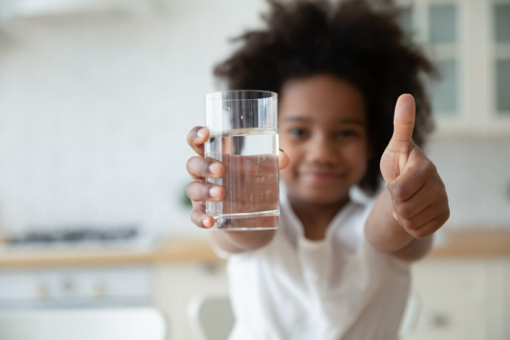Little girl holding glass of water with one hand and giving a thumbs up with the other